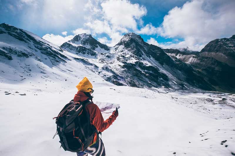 someone looking at a map on top of a snow capped mountain
